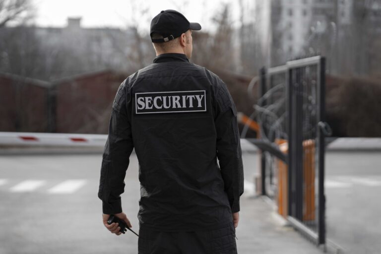 Security guard standing at a gated entrance – cost-benefit comparison of remote video monitoring vs on-site guards by Monitex Security